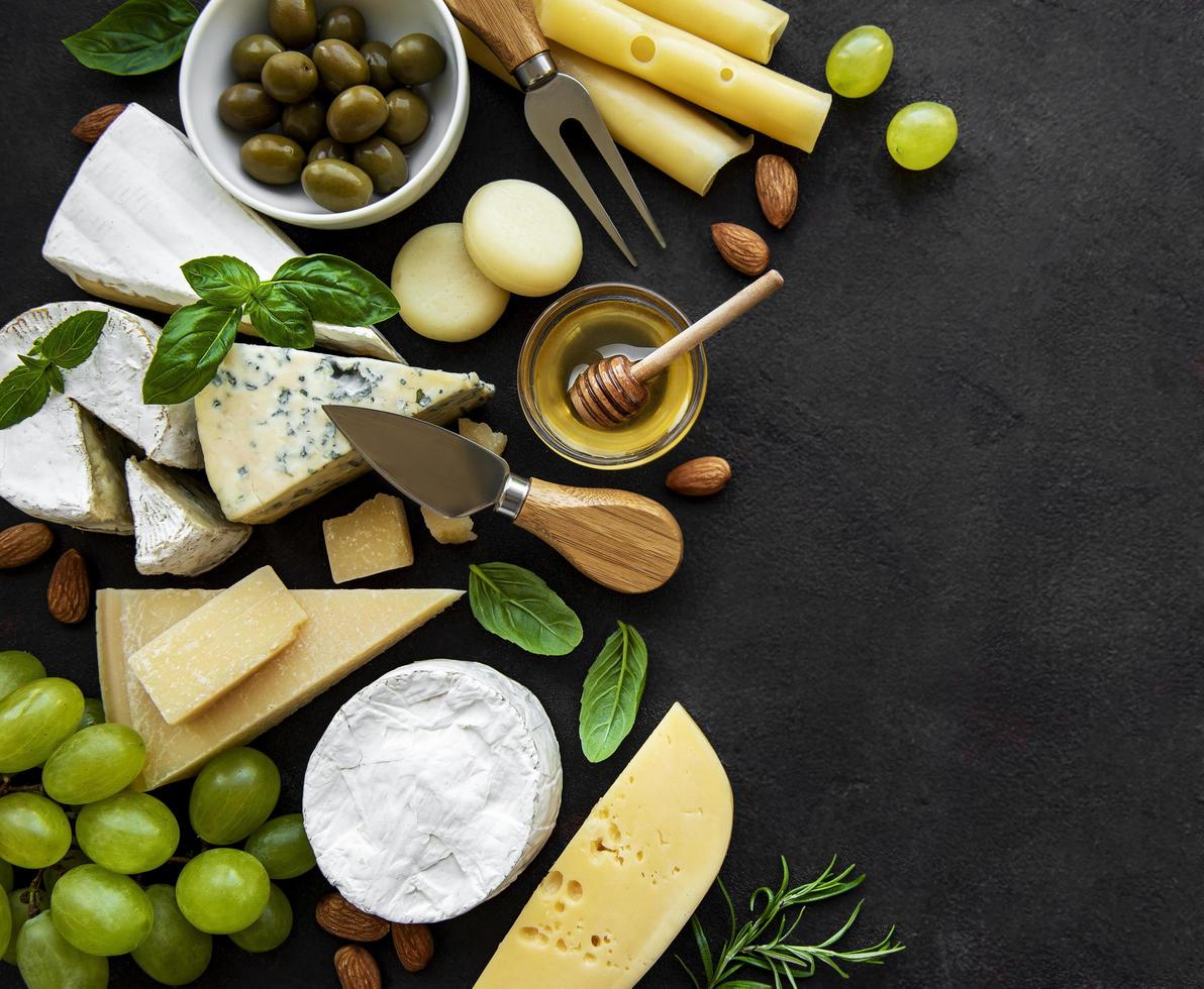 Various types of cheese, grapes, honey, and snacks on a black concrete background photo