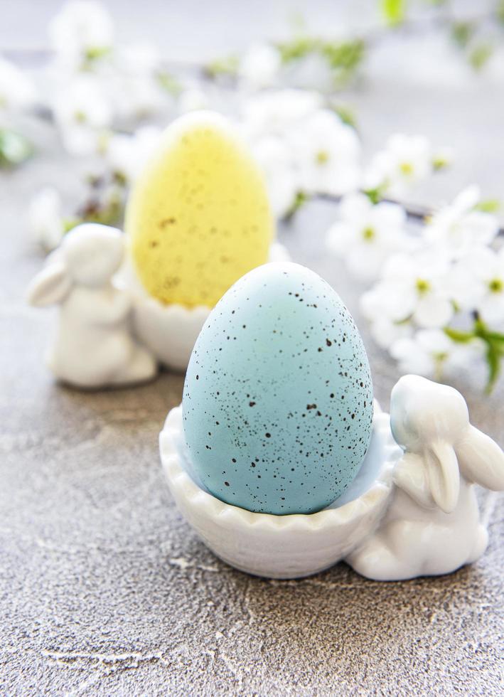 Colorful Easter eggs in a stand with ceramic Easter bunny figurines and spring blossom on gray concrete background photo