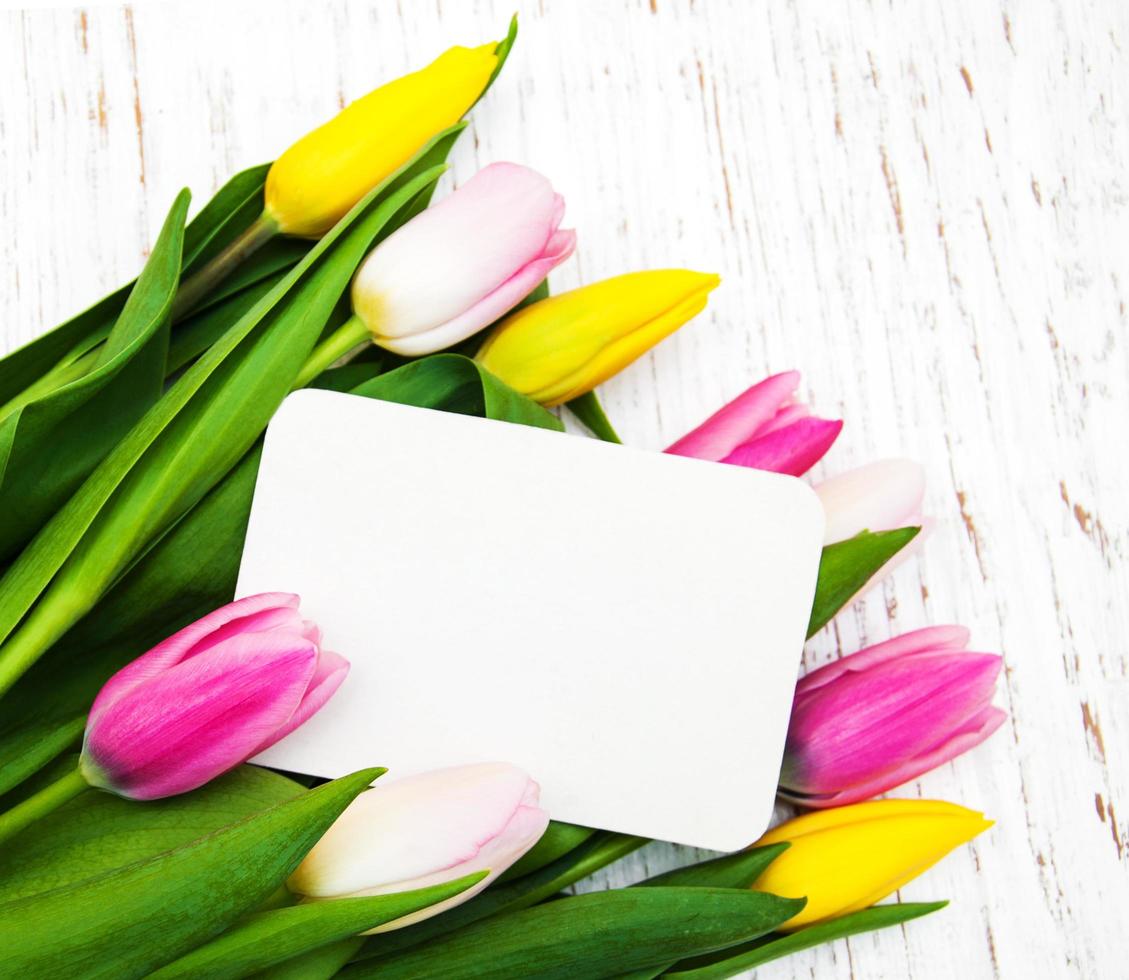 Tulipanes rosados y amarillos con una tarjeta sobre un fondo de madera blanca foto