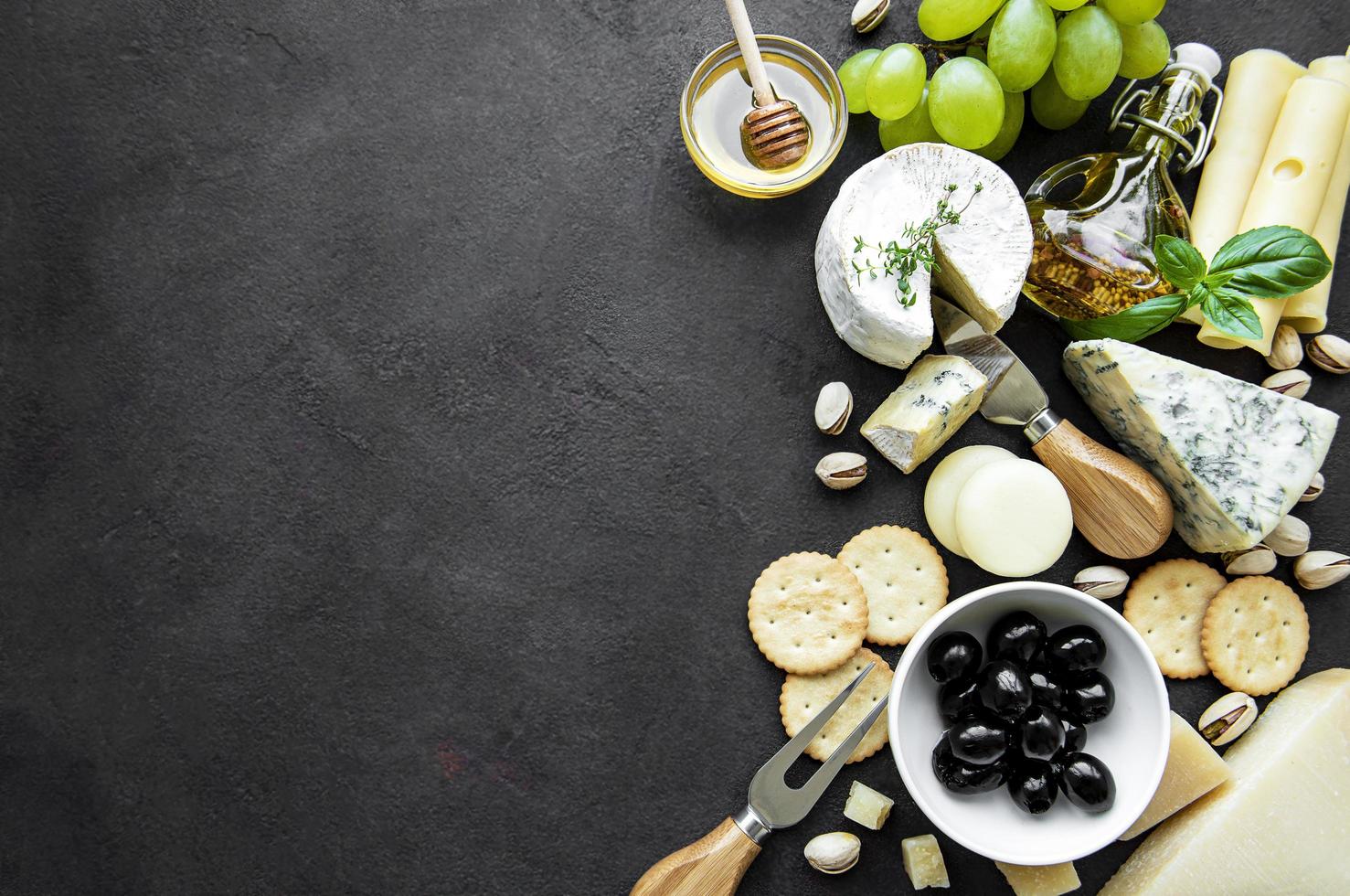 Various types of cheese, grapes, honey, and snacks on a black concrete background photo