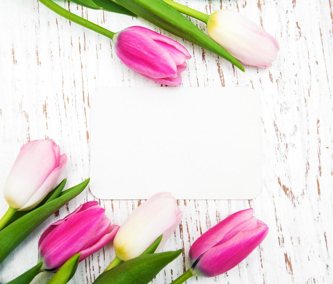 Pink and yellow tulips with a card on a white wooden background photo