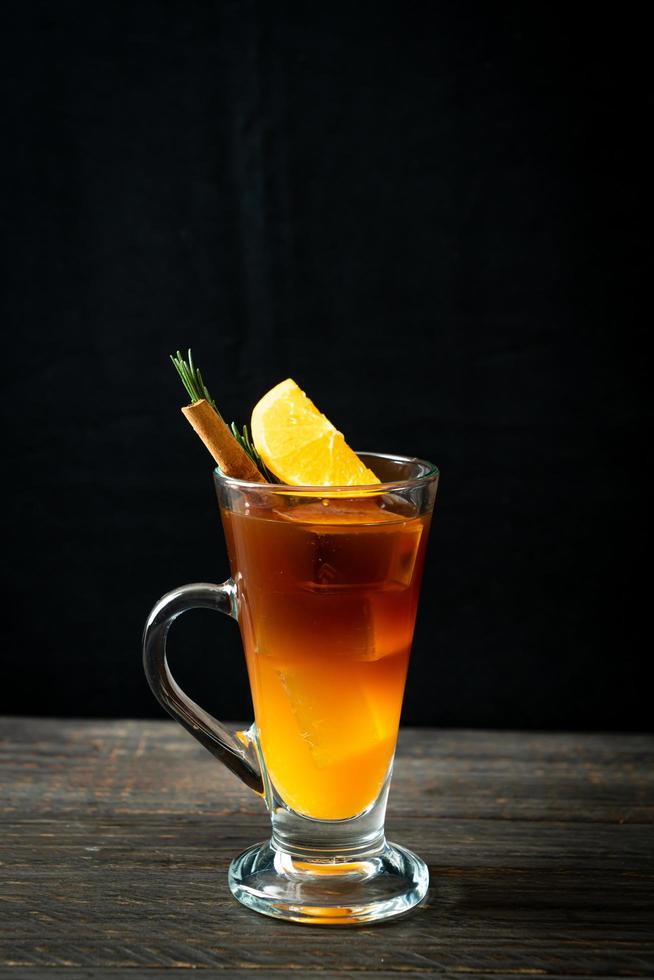 un vaso de café negro americano helado y una capa de jugo de naranja y limón decorado con romero y canela foto