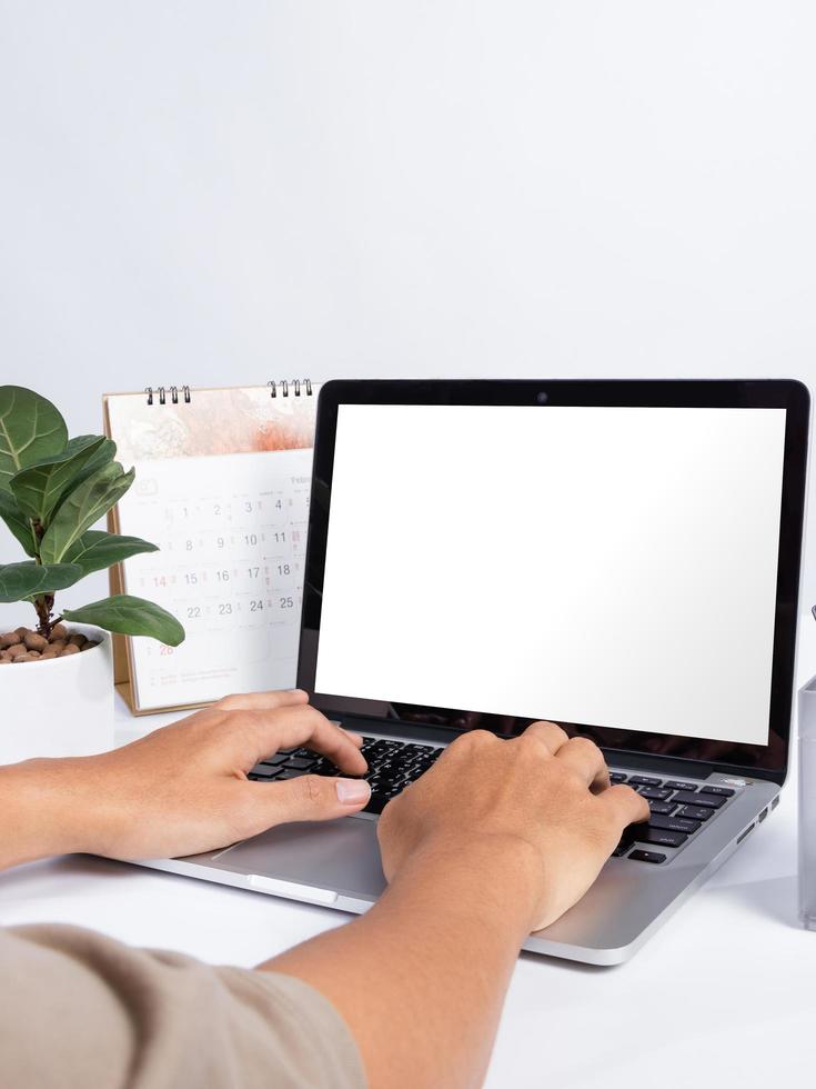 Hombre usando una maqueta de pantalla en blanco de computadora portátil en el escritorio de oficina blanco foto