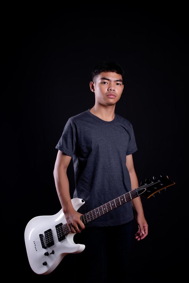 Young man in black leather jacket with electric guitar against black background in studio photo