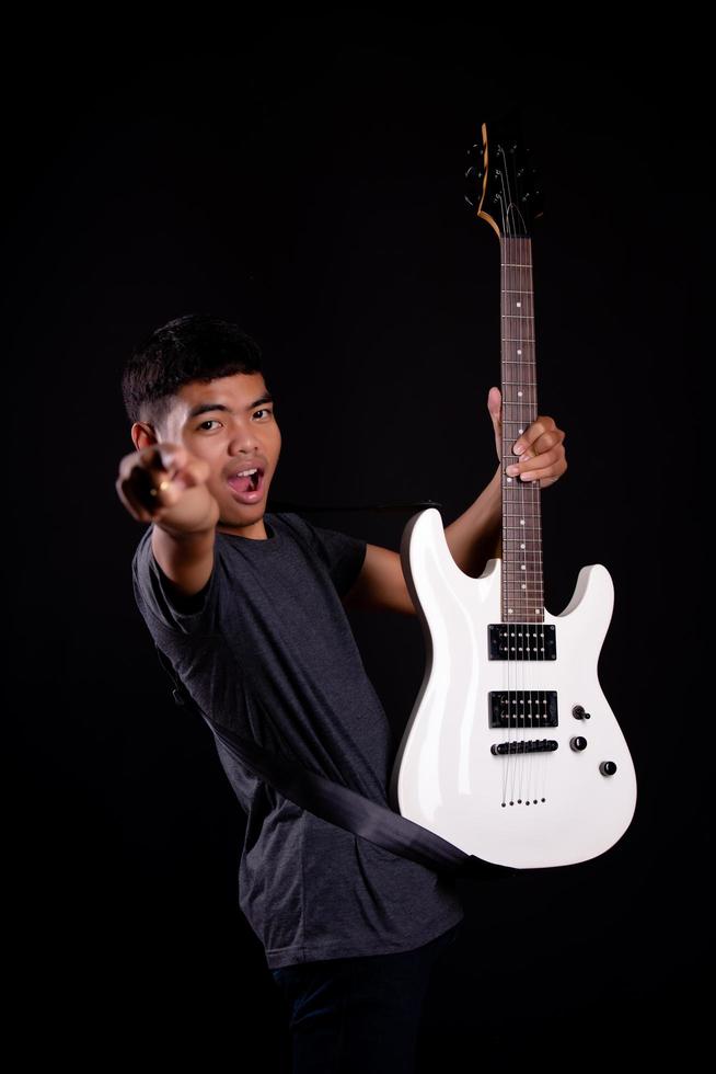 Joven en chaqueta de cuero negro con guitarra eléctrica contra fondo negro en studio foto