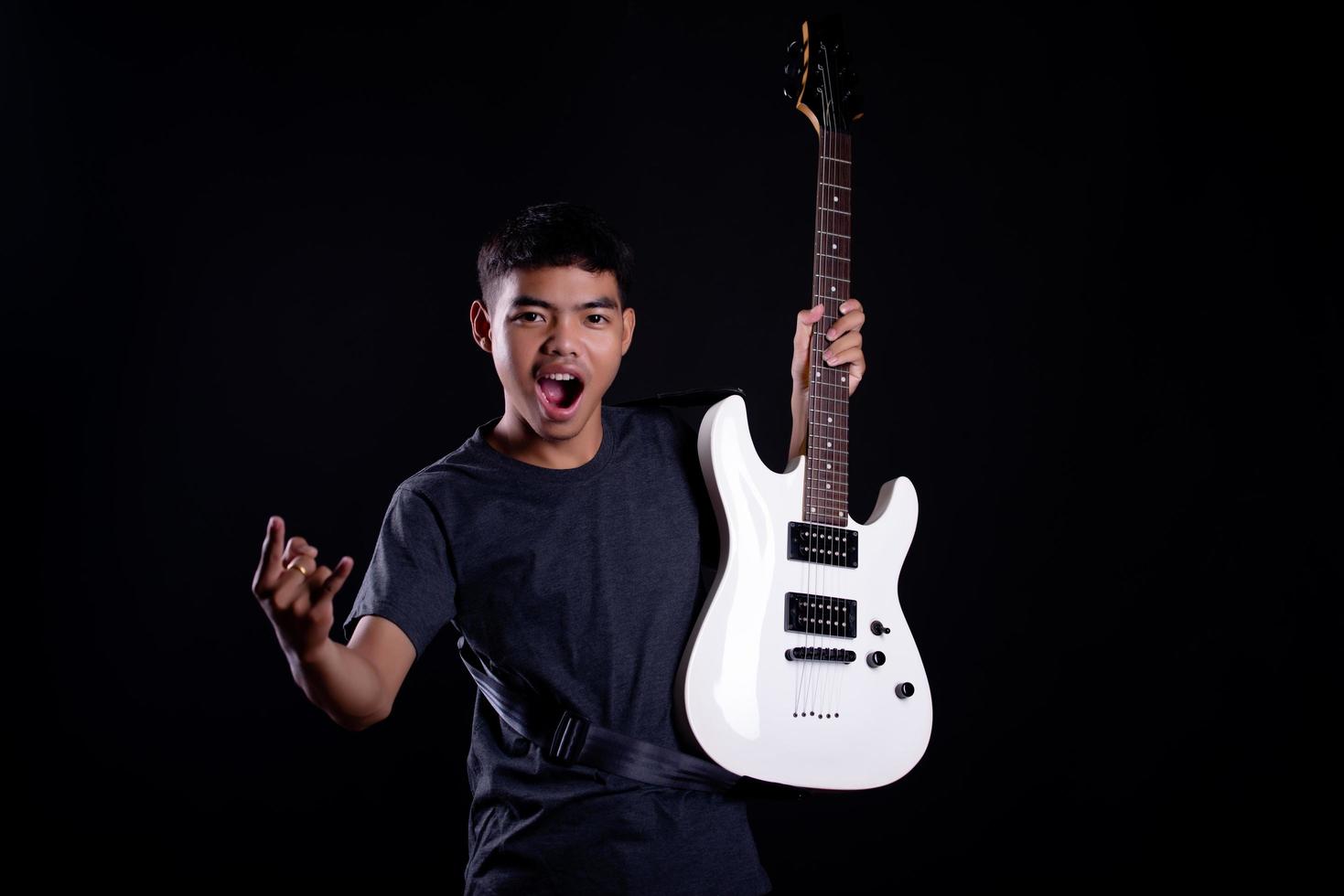 Young man in black leather jacket with electric guitar against black background in studio photo