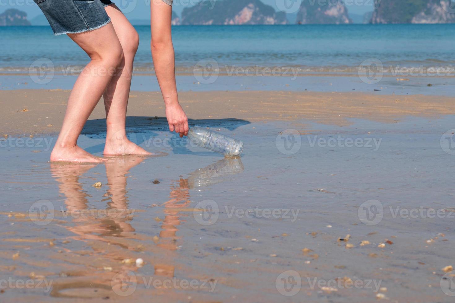 Young asian woman collecting used plastic bottle from the beach to save environment and marine ecosystem photo
