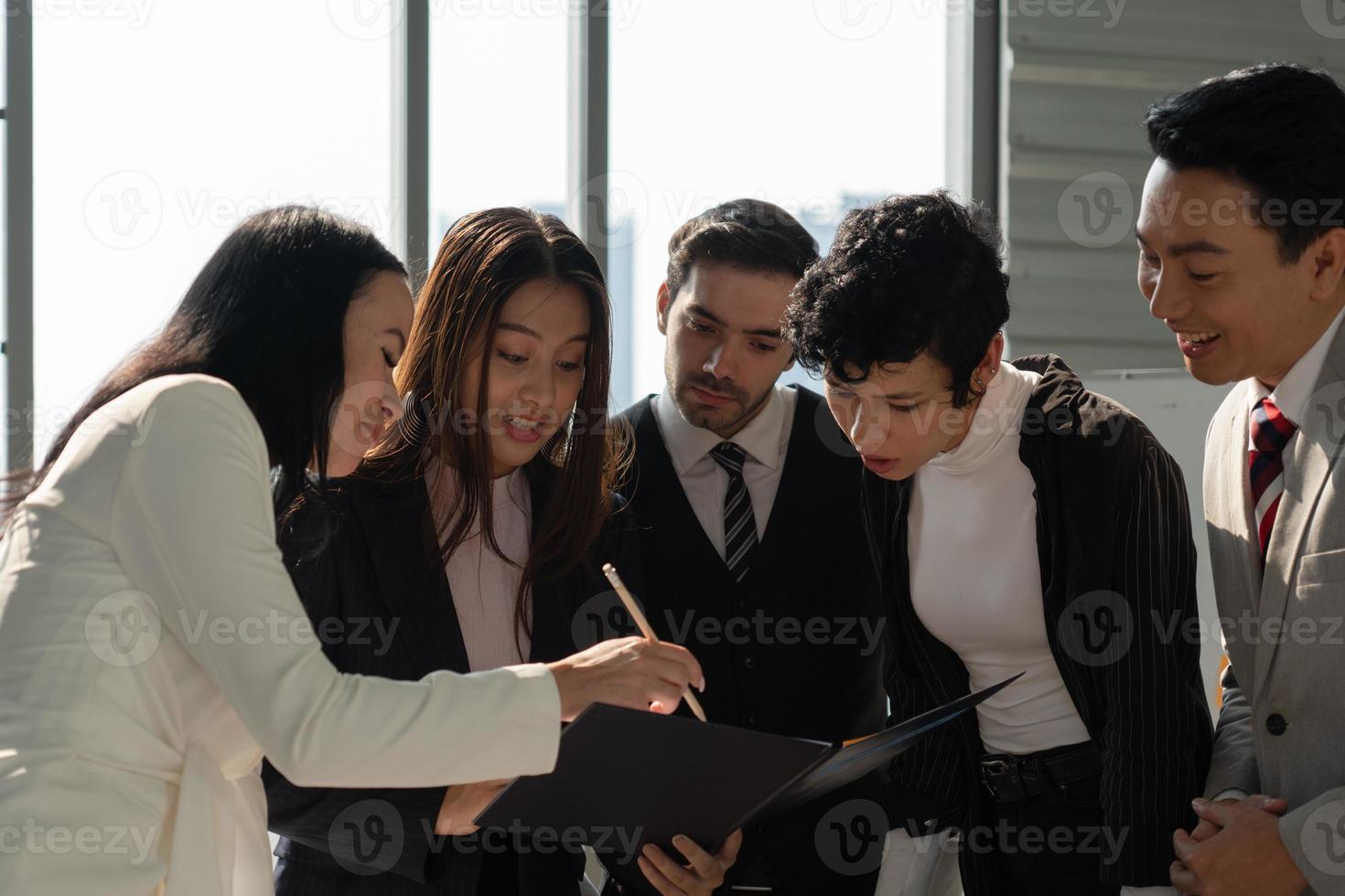 Equipo de negocios internacionales que incluye personas caucásicas y asiáticas de pie cerca de la ventana en la oficina y discutiendo sobre el proyecto foto