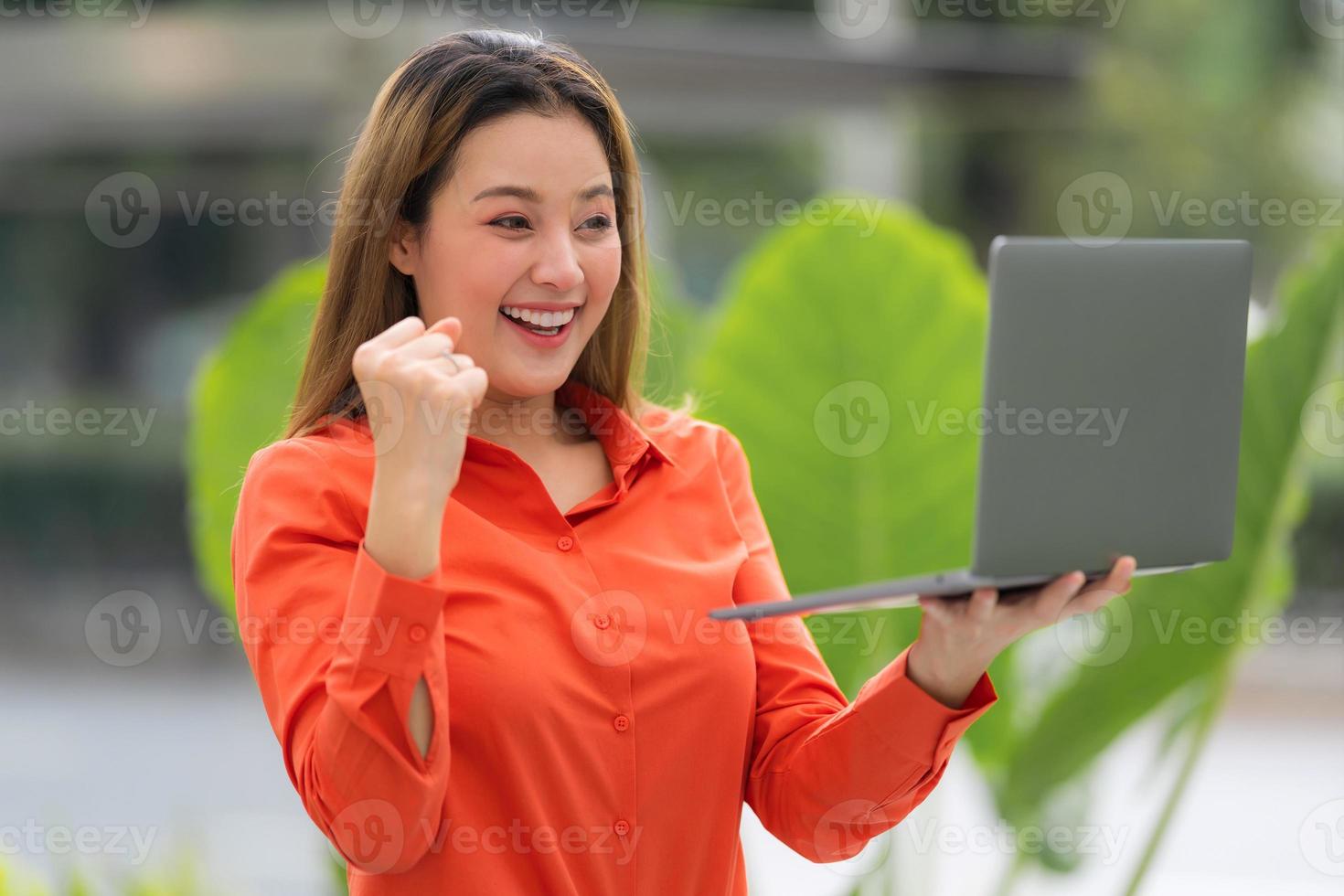 Beautiful young woman with happy screaming surprised face holding laptop in a city park photo