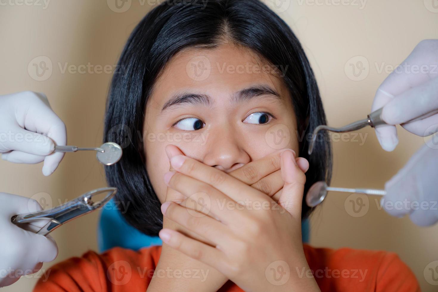 Chica asustada por dentistas cubre su boca en el consultorio del dentista foto