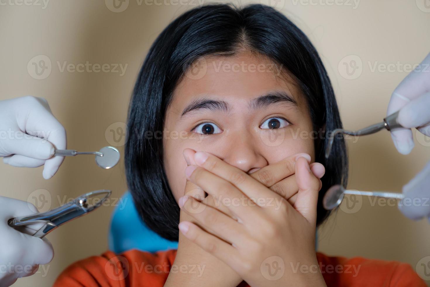 Chica asustada por dentistas cubre su boca en el consultorio del dentista foto