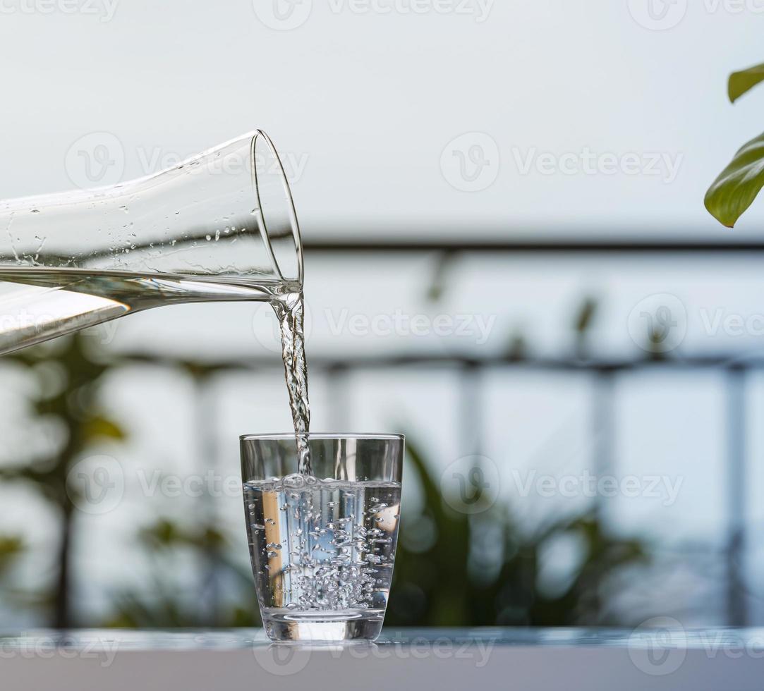 Verter agua potable de botella en vaso en casa de jardín foto