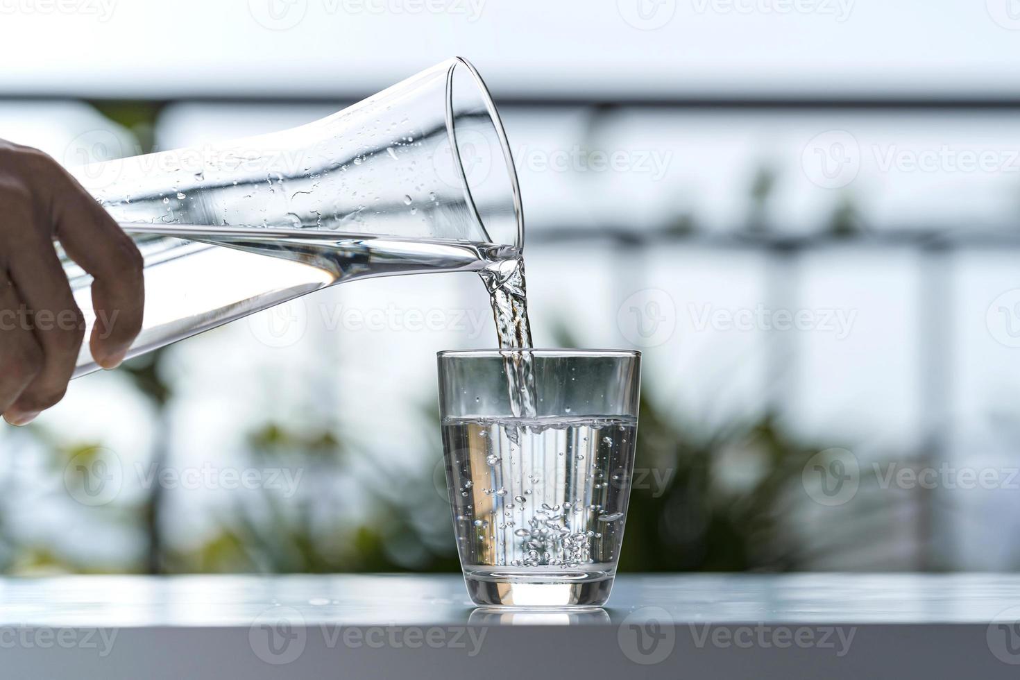 Verter agua potable de botella en vaso en casa de jardín foto