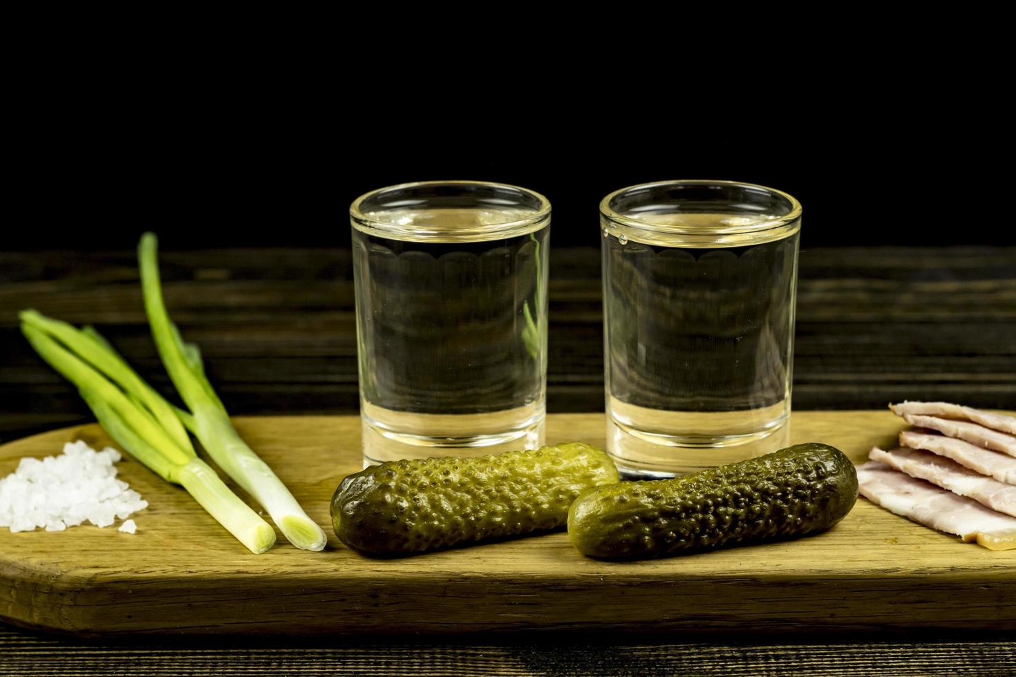 vodka and two glasses and cucumbers with bacon and onions photo