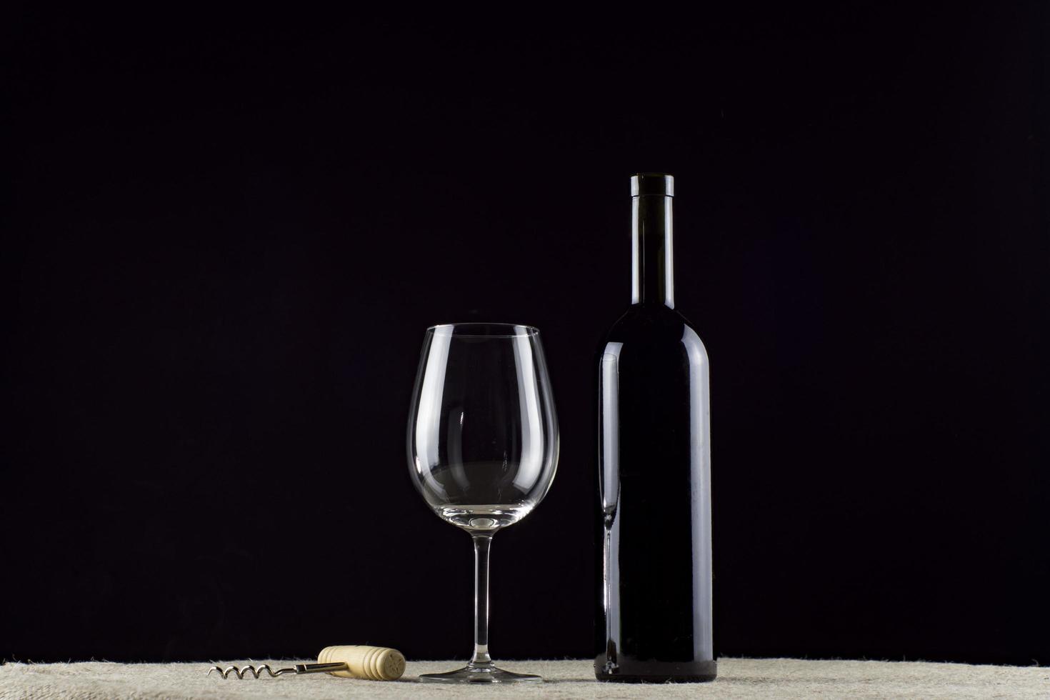 Botella de vino de vidrio y sacacorchos sobre un fondo negro papel tapiz foto