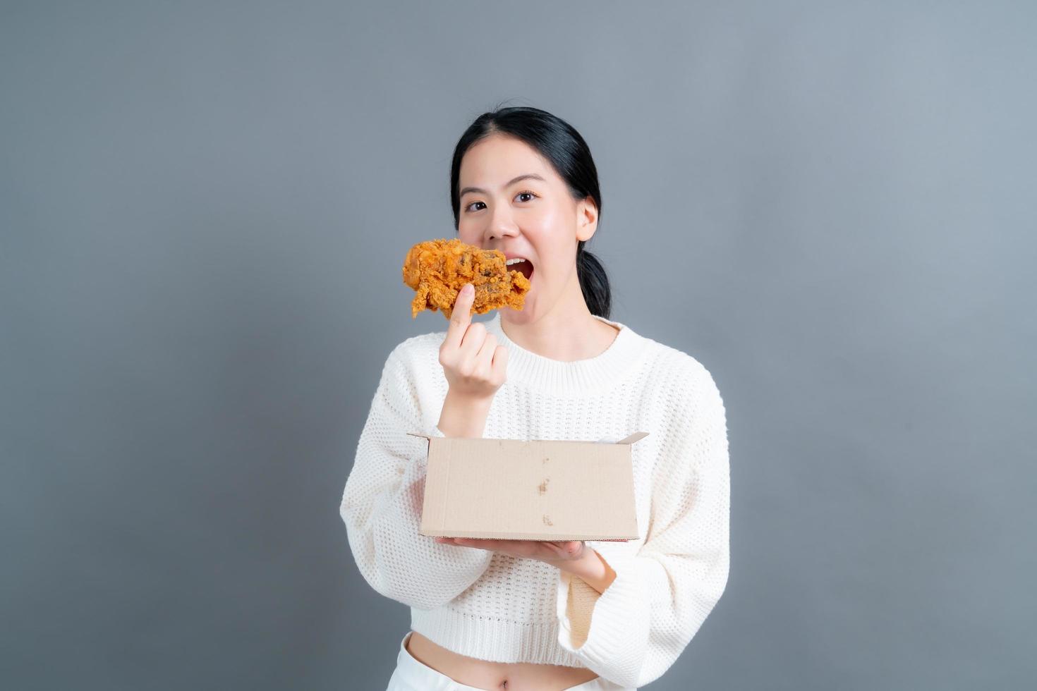 Joven mujer asiática con cara feliz y disfruta comiendo pollo frito foto