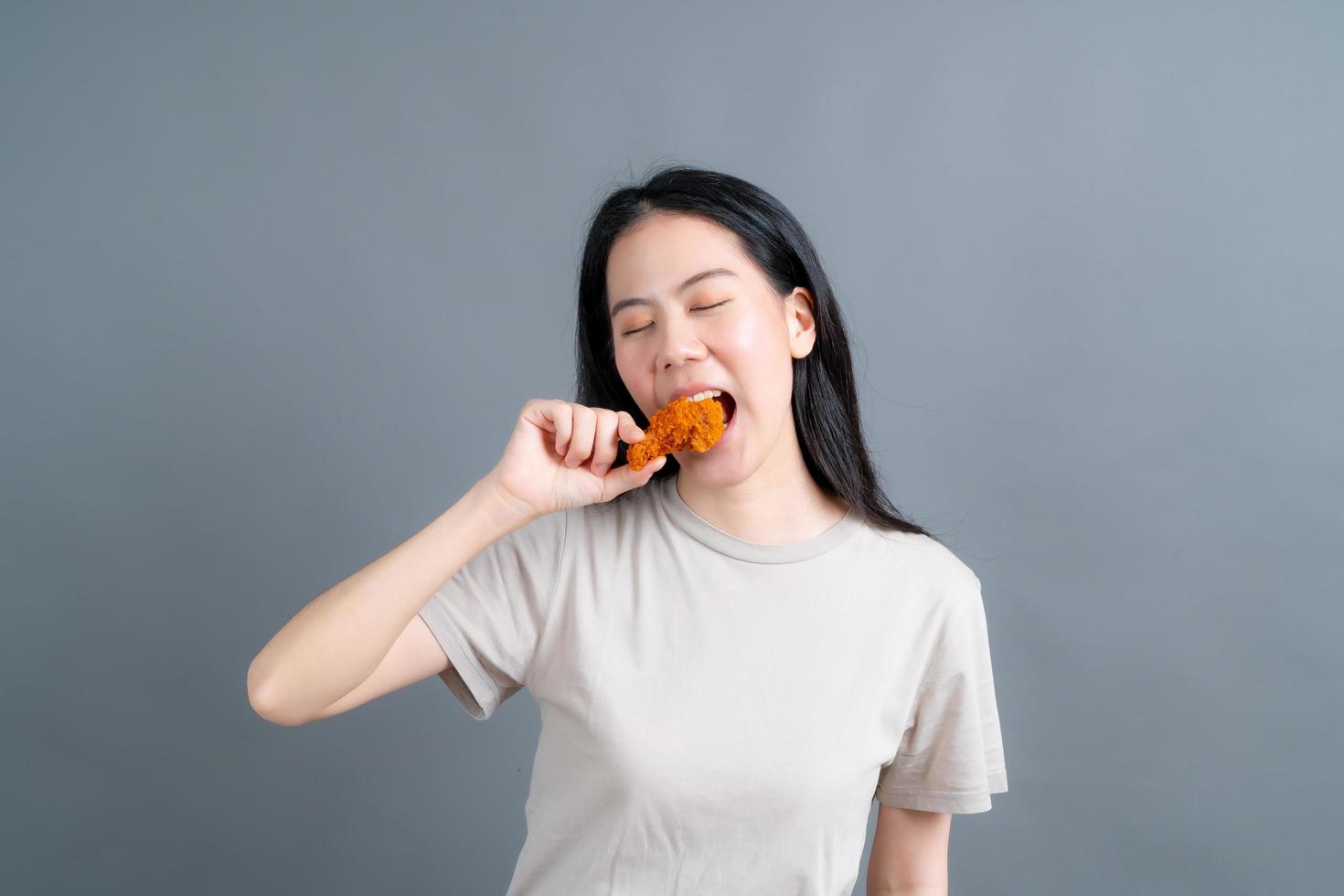 Joven mujer asiática con cara feliz y disfruta comiendo pollo frito foto