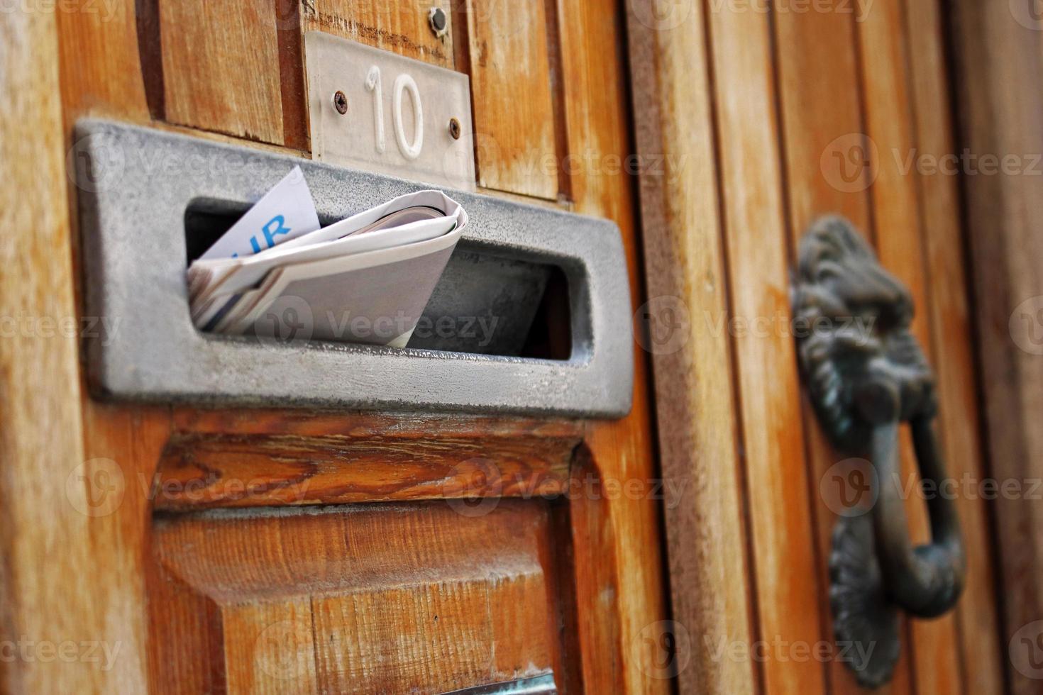 Mail box filled with rolled spam newspaper in old wooden door photo