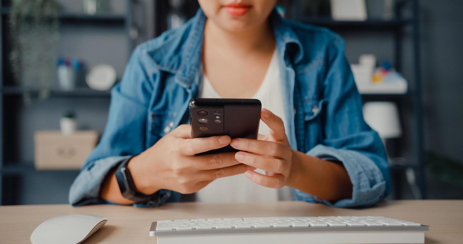 Freelancer Asia lady casual wear using smartphone shopping online via website while sitting at desk in living room photo