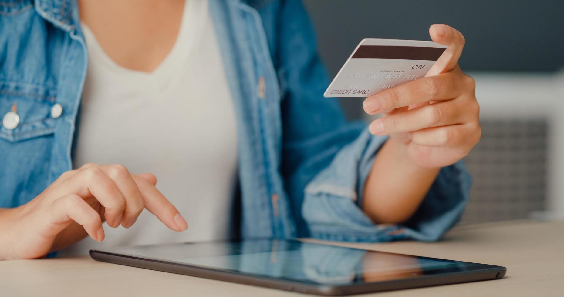 Young asia lady using tablet order online shopping product and paying bills with credit card in living room interior photo