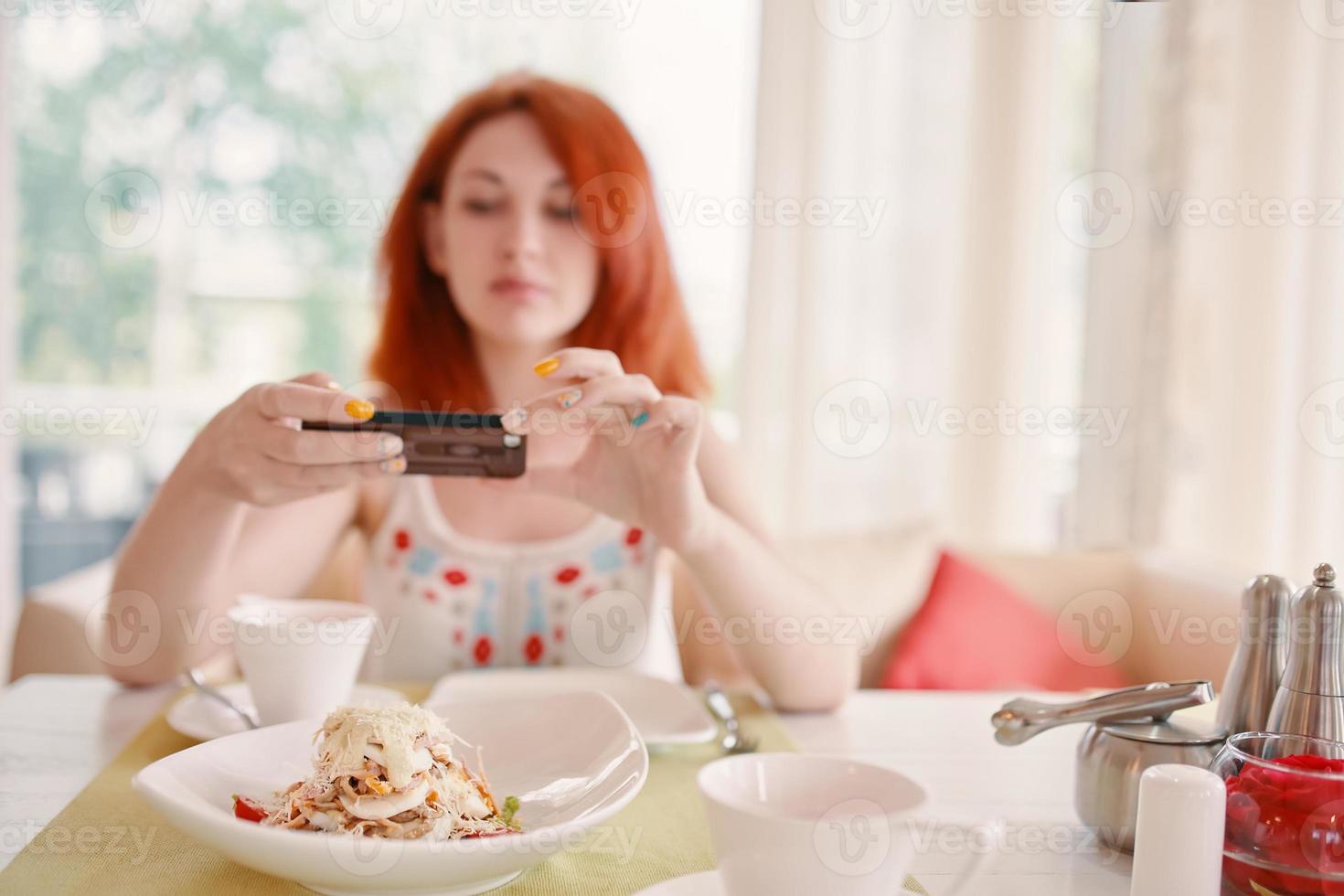 Mujer de pelo rojo toma fotos de ensalada en la cámara del teléfono inteligente