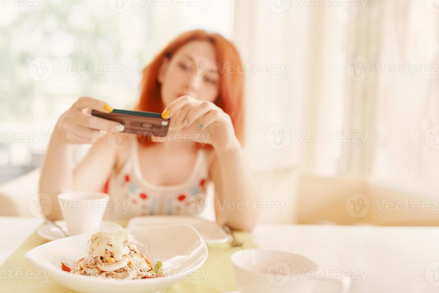 Redhaired woman takes photos of salad on smartphone camera