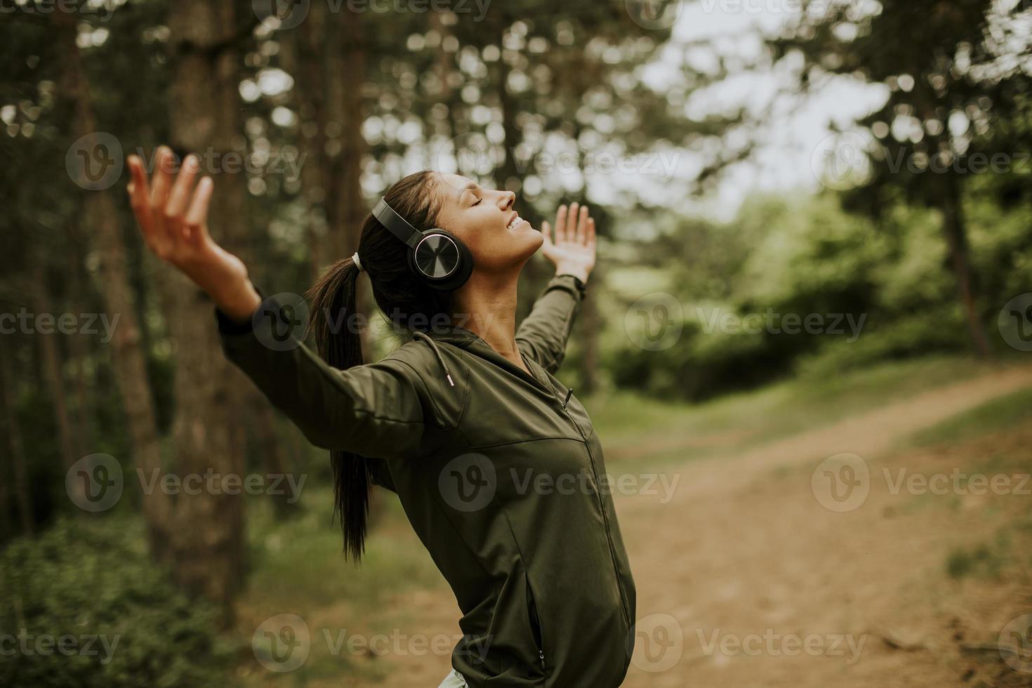Young woman with earphones preading her arms in the forest because she enjoys training outside photo