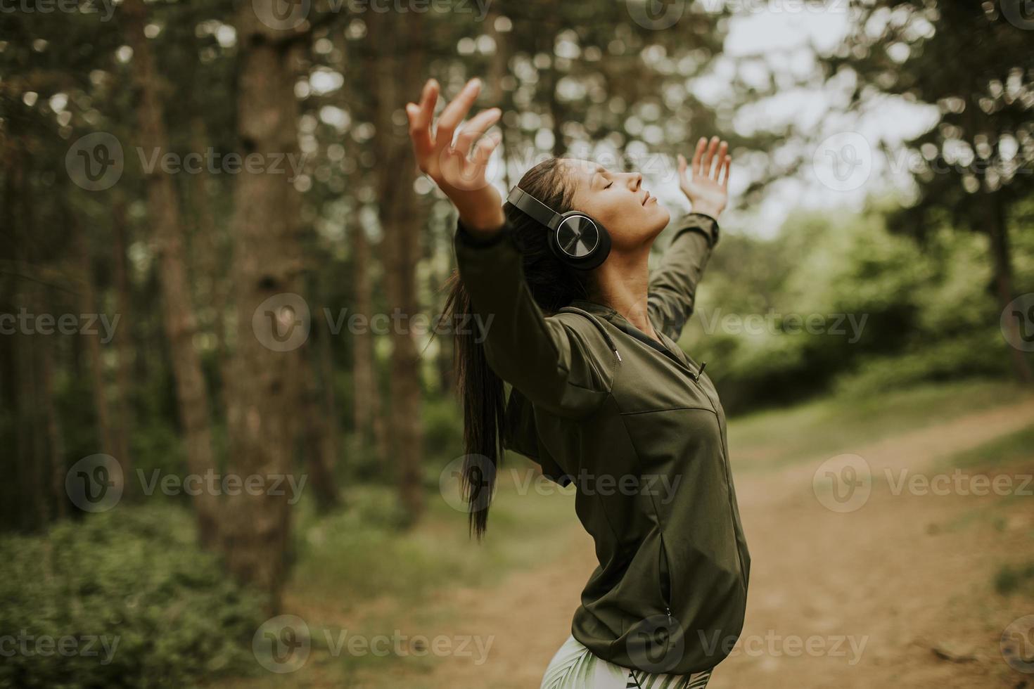 Mujer joven con auriculares predicando sus brazos en el bosque porque le gusta entrenar al aire libre foto