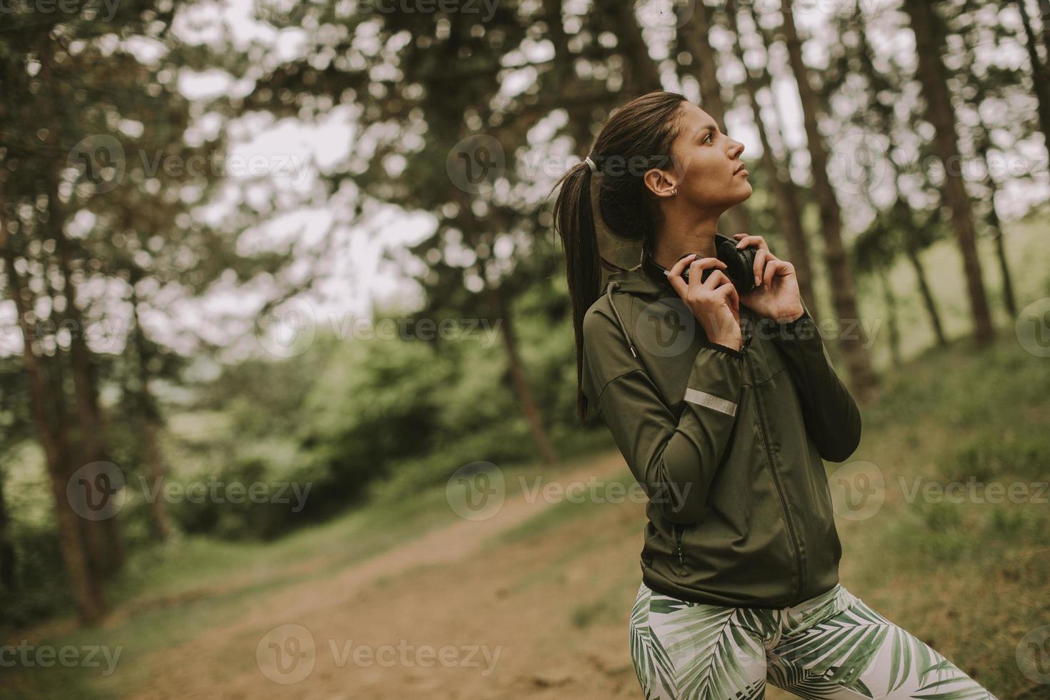 Young beautiful female runner listening to music and taking a break after jogging in a forest photo