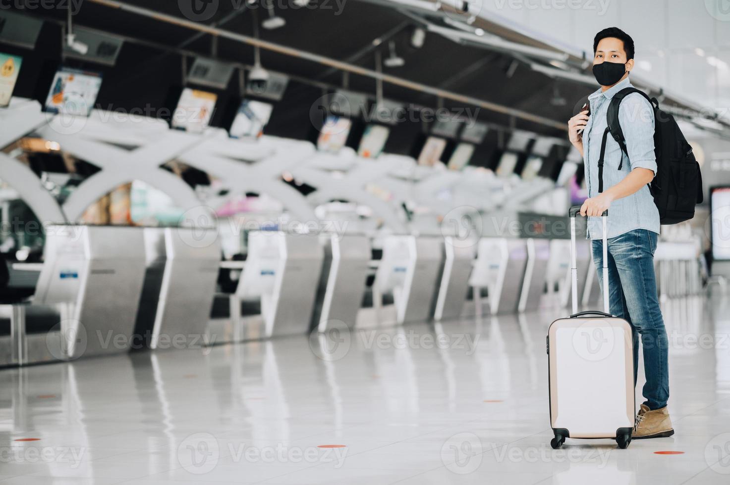 Asian man traveler wearing mask for protect from coronavirus standing with luggage photo