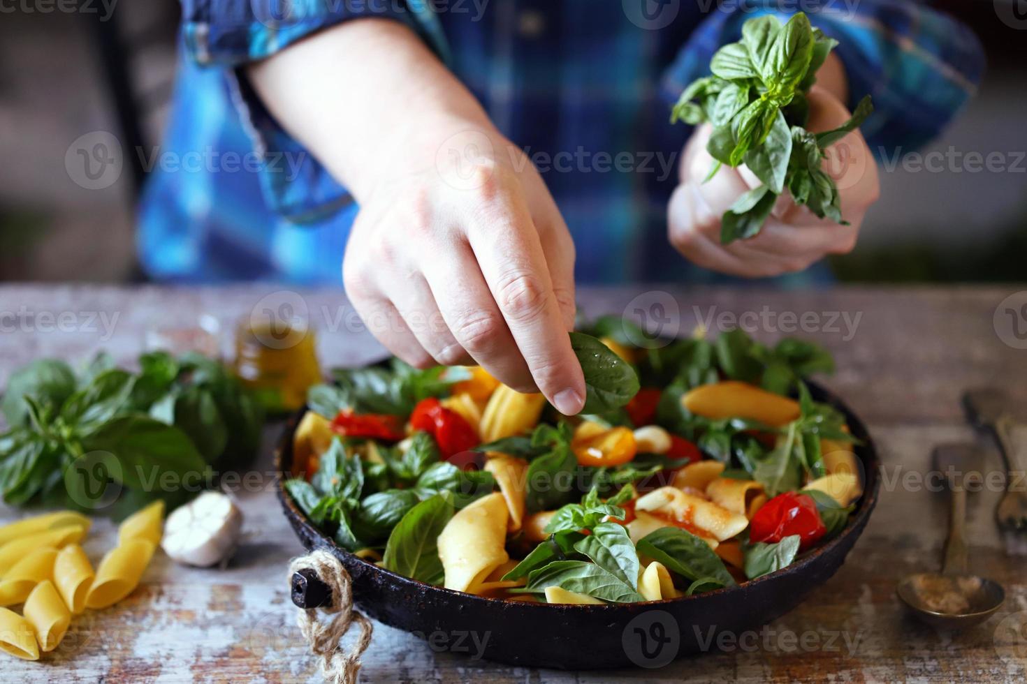Chef mixes pasta with basil and spices in a pan photo
