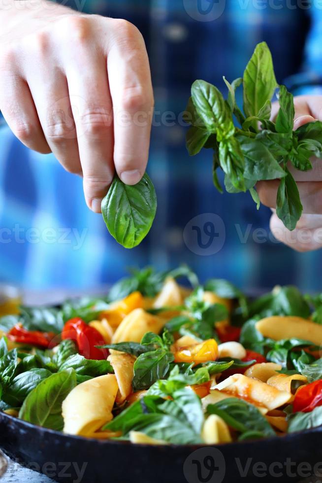 Chef mezcla pasta con albahaca y especias en una sartén foto