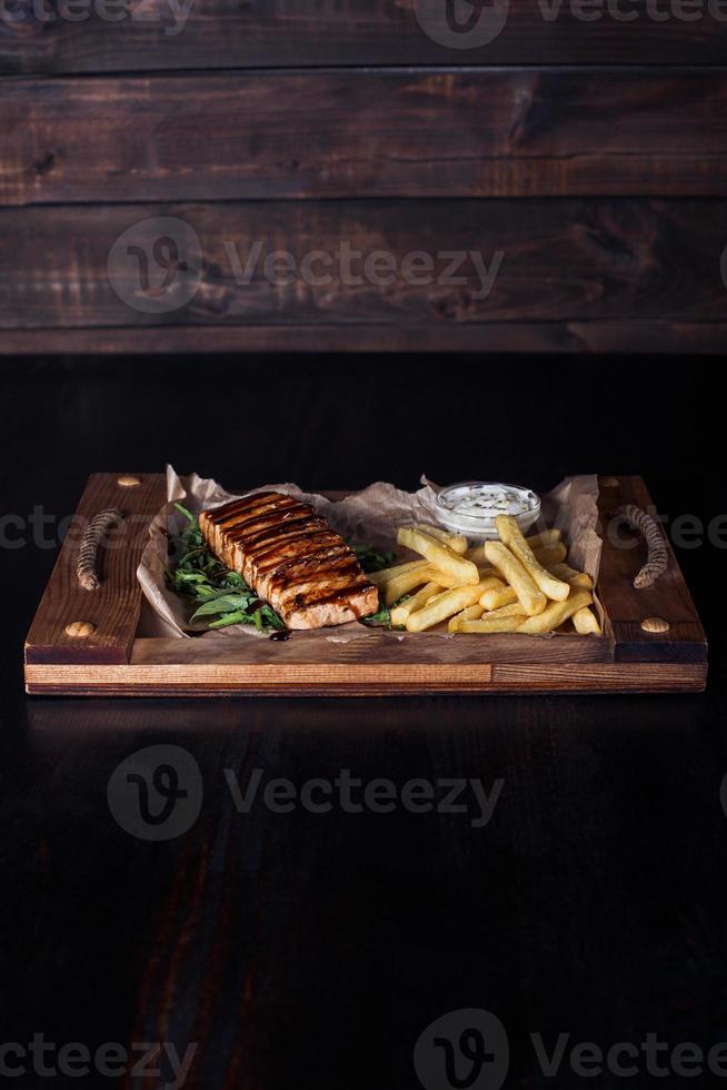 salmon fillet steak with french fries on a wooden tray, beautiful serving, dark background photo