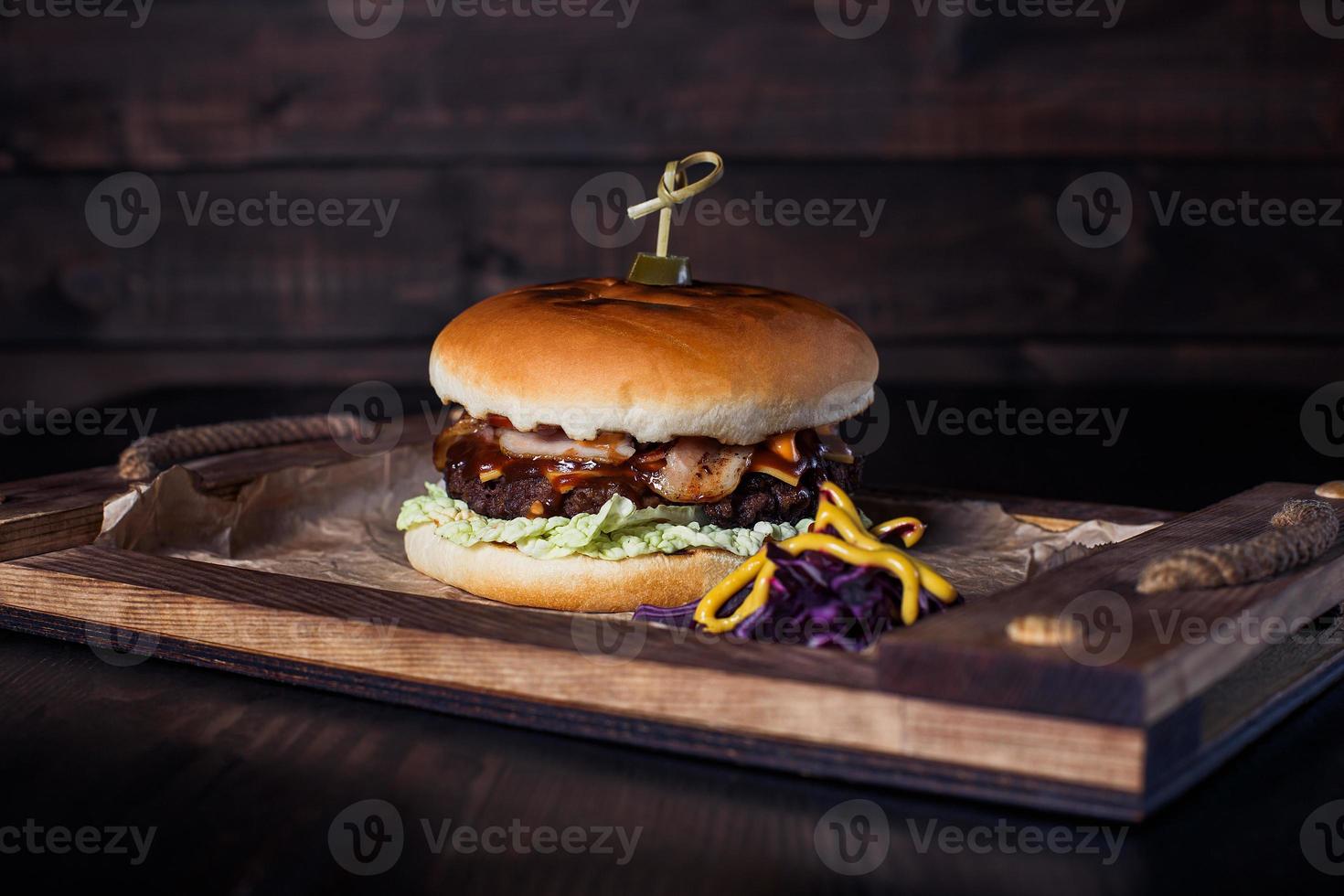 Hamburguesa con queso en una bandeja de madera en un restaurante, sobre un fondo oscuro foto