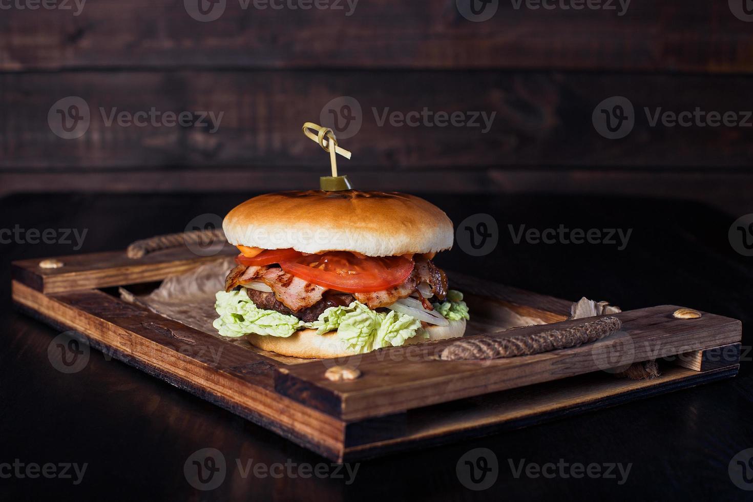 Hamburguesa con queso en una bandeja de madera en un restaurante, sobre un fondo oscuro foto