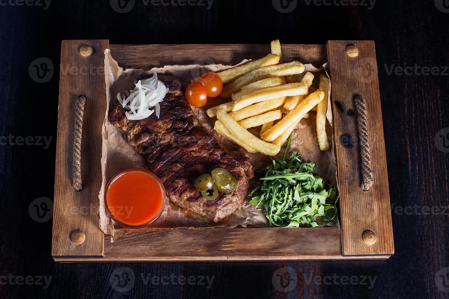 Filete de ternera con papas fritas en una bandeja de madera, hermosa porción, fondo oscuro foto