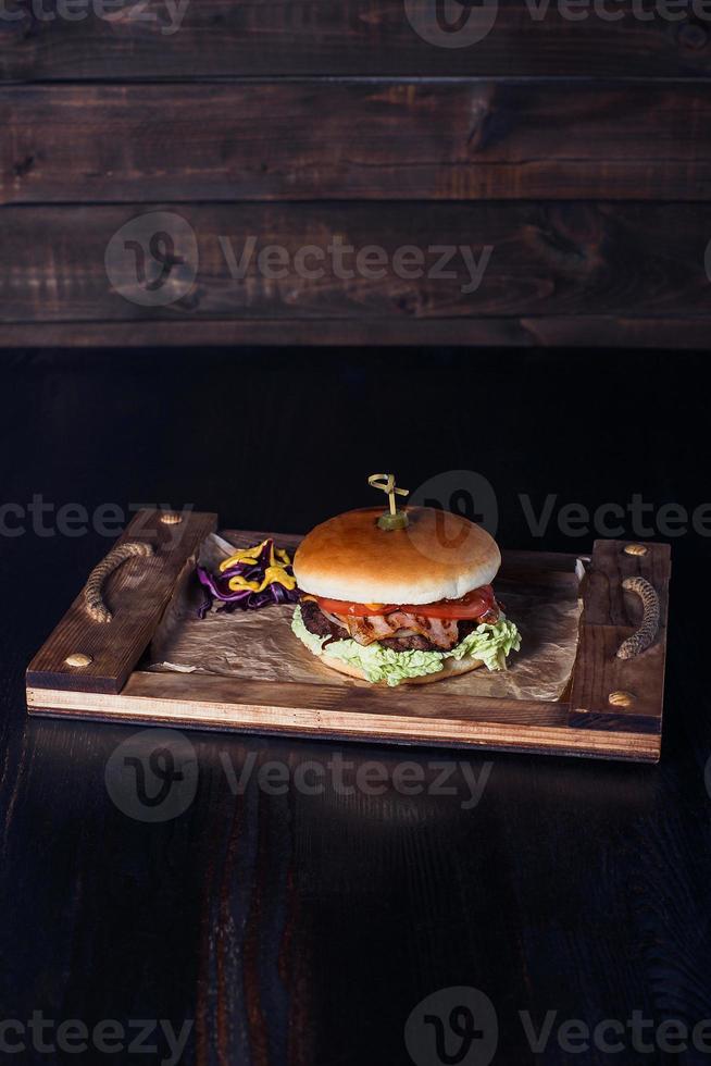 Hamburguesa con queso en una bandeja de madera en un restaurante, sobre un fondo oscuro foto