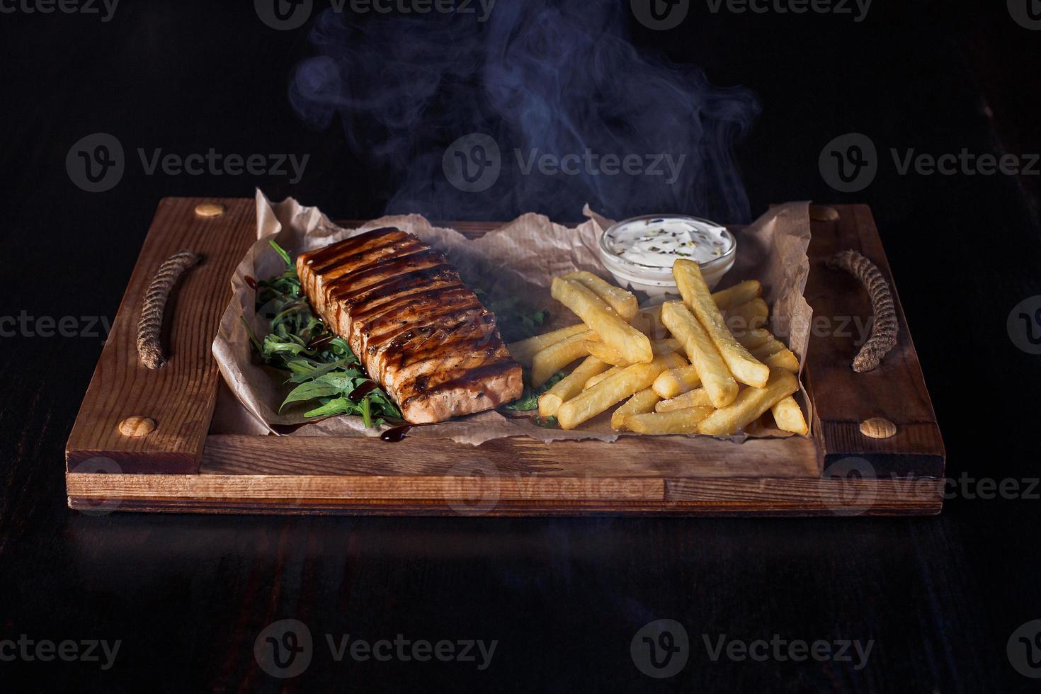 Filete de salmón con papas fritas en una bandeja de madera, hermosa porción, fondo oscuro foto