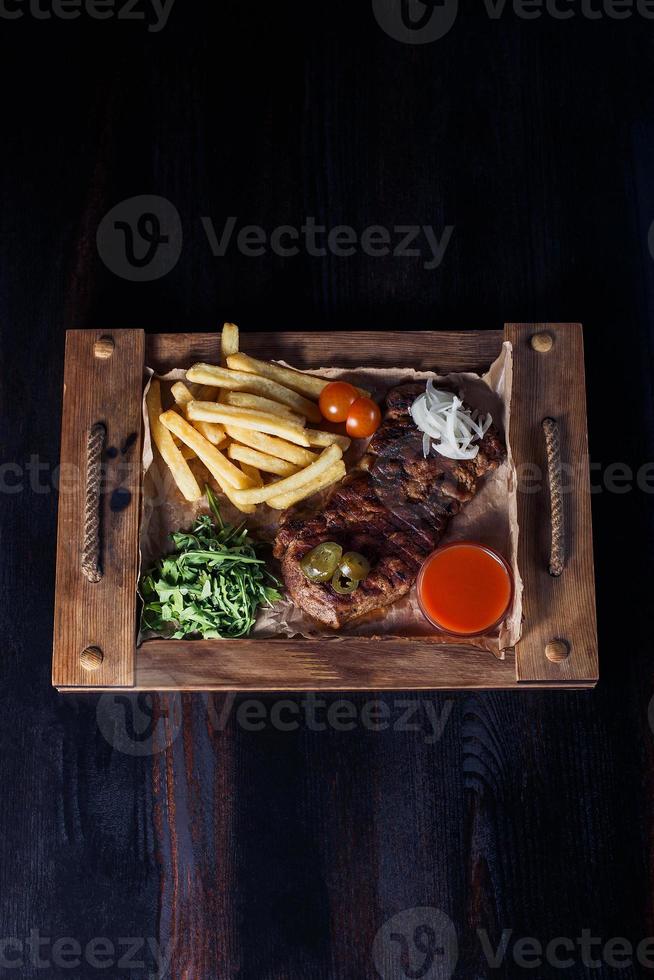 Filete de ternera con papas fritas en una bandeja de madera, hermosa porción, fondo oscuro foto