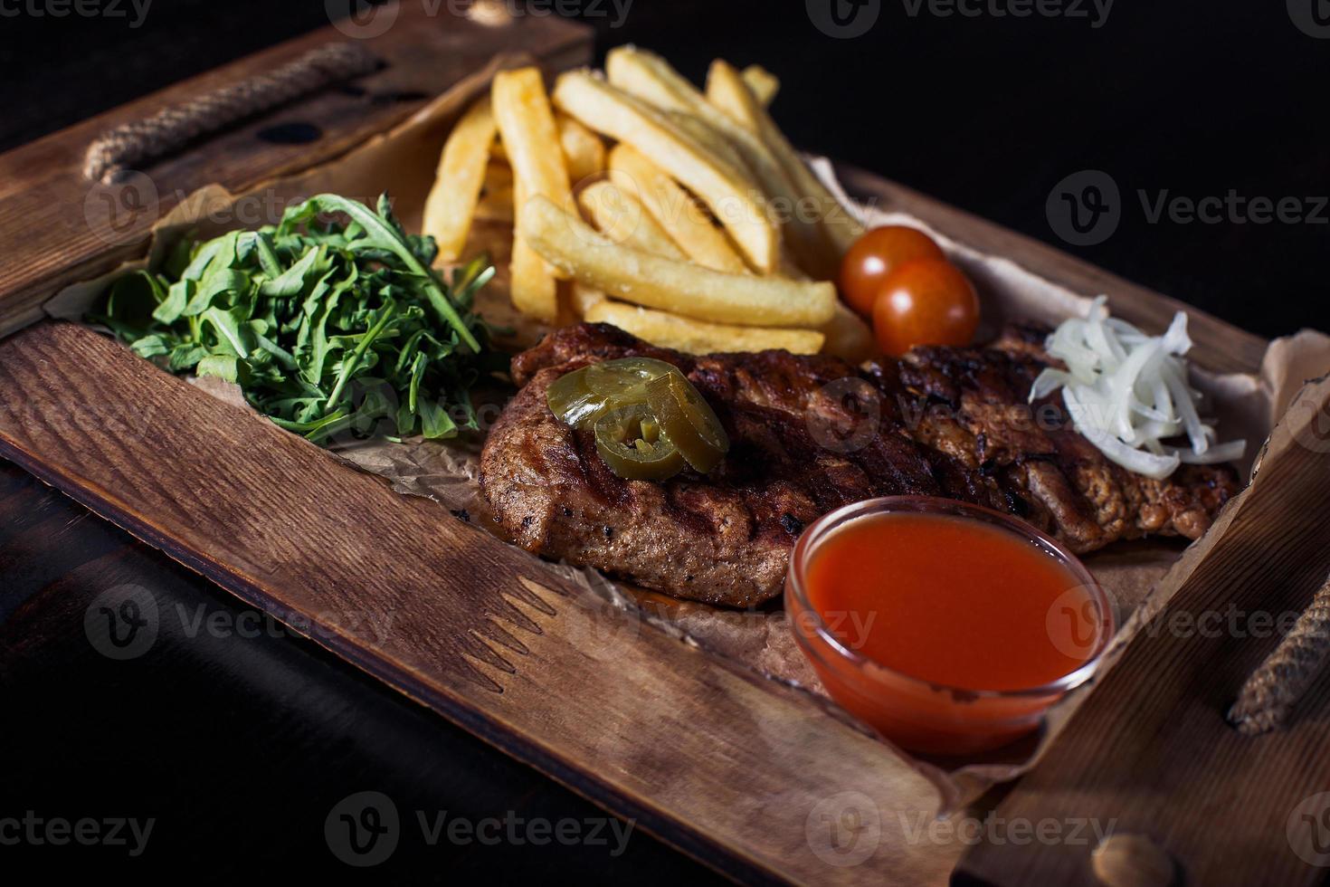 Filete de ternera con papas fritas en una bandeja de madera, hermosa porción, fondo oscuro foto