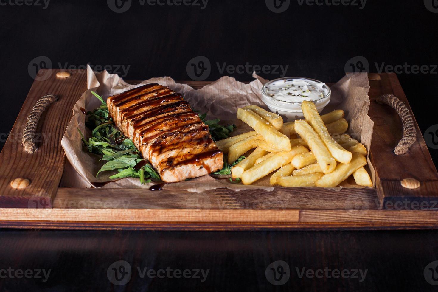 salmon fillet steak with french fries on a wooden tray, beautiful serving, dark background photo