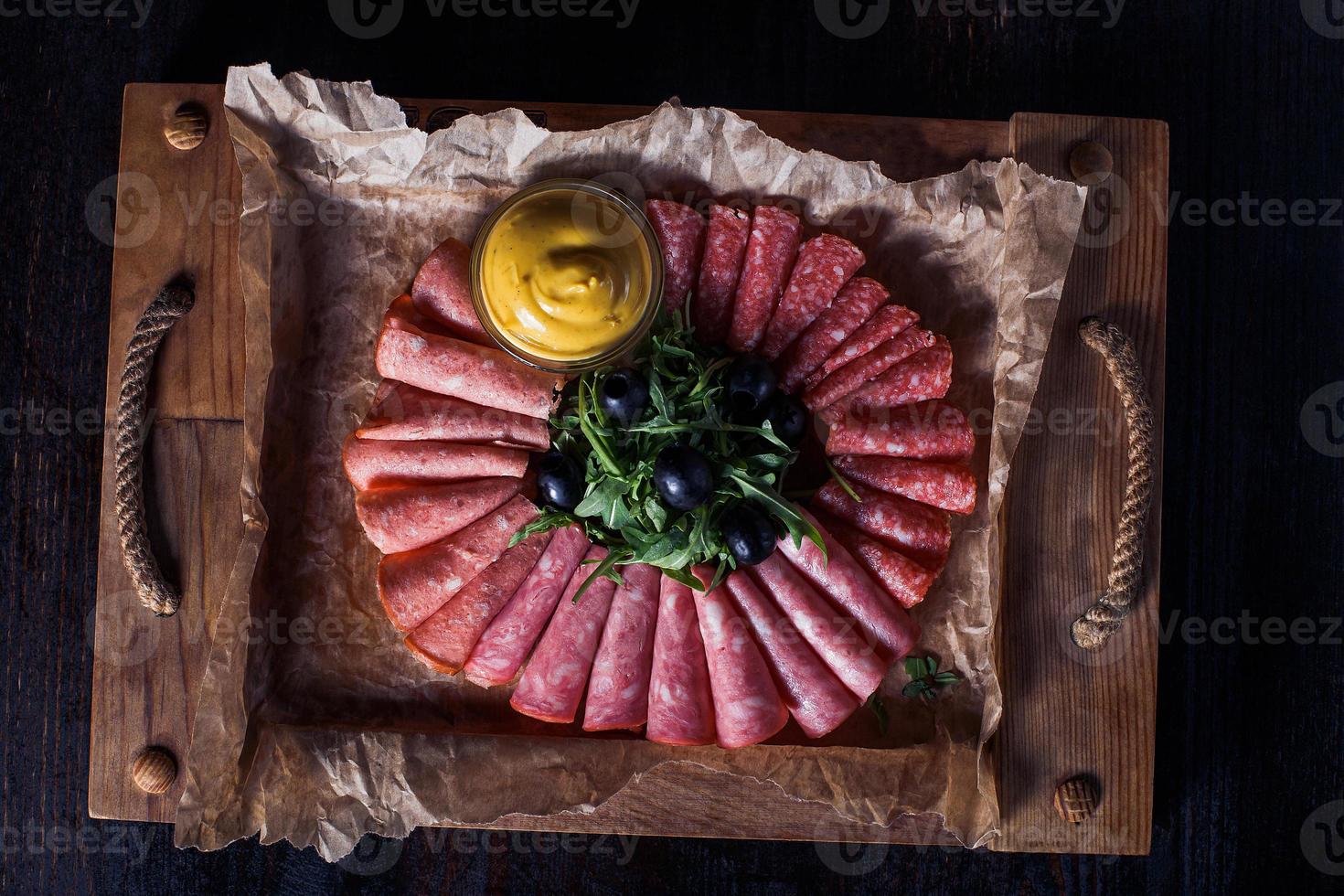 Salchicha cortada con hierbas y salsa en una bandeja de madera, hermosa porción, fondo oscuro foto