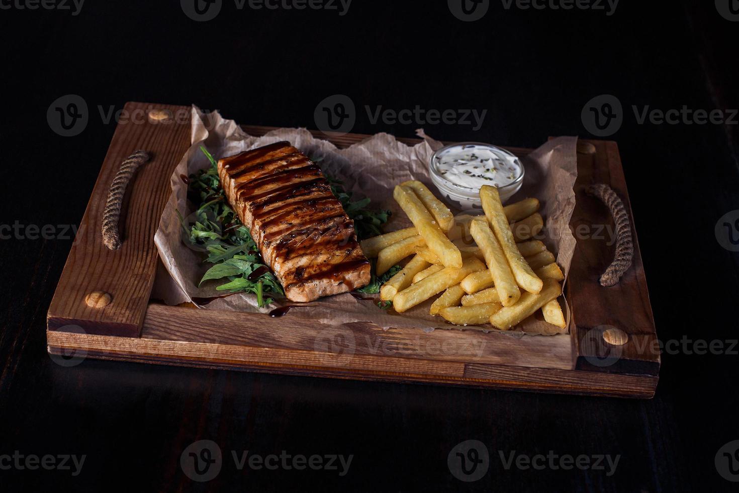 salmon fillet steak with french fries on a wooden tray, beautiful serving, dark background photo