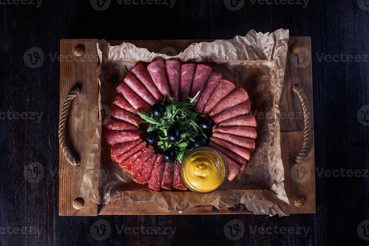 Salchicha cortada con hierbas y salsa en una bandeja de madera, hermosa porción, fondo oscuro foto