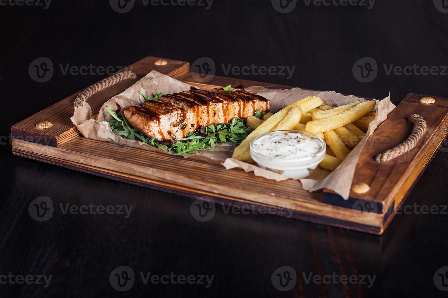 Filete de salmón con papas fritas en una bandeja de madera, hermosa porción, fondo oscuro foto