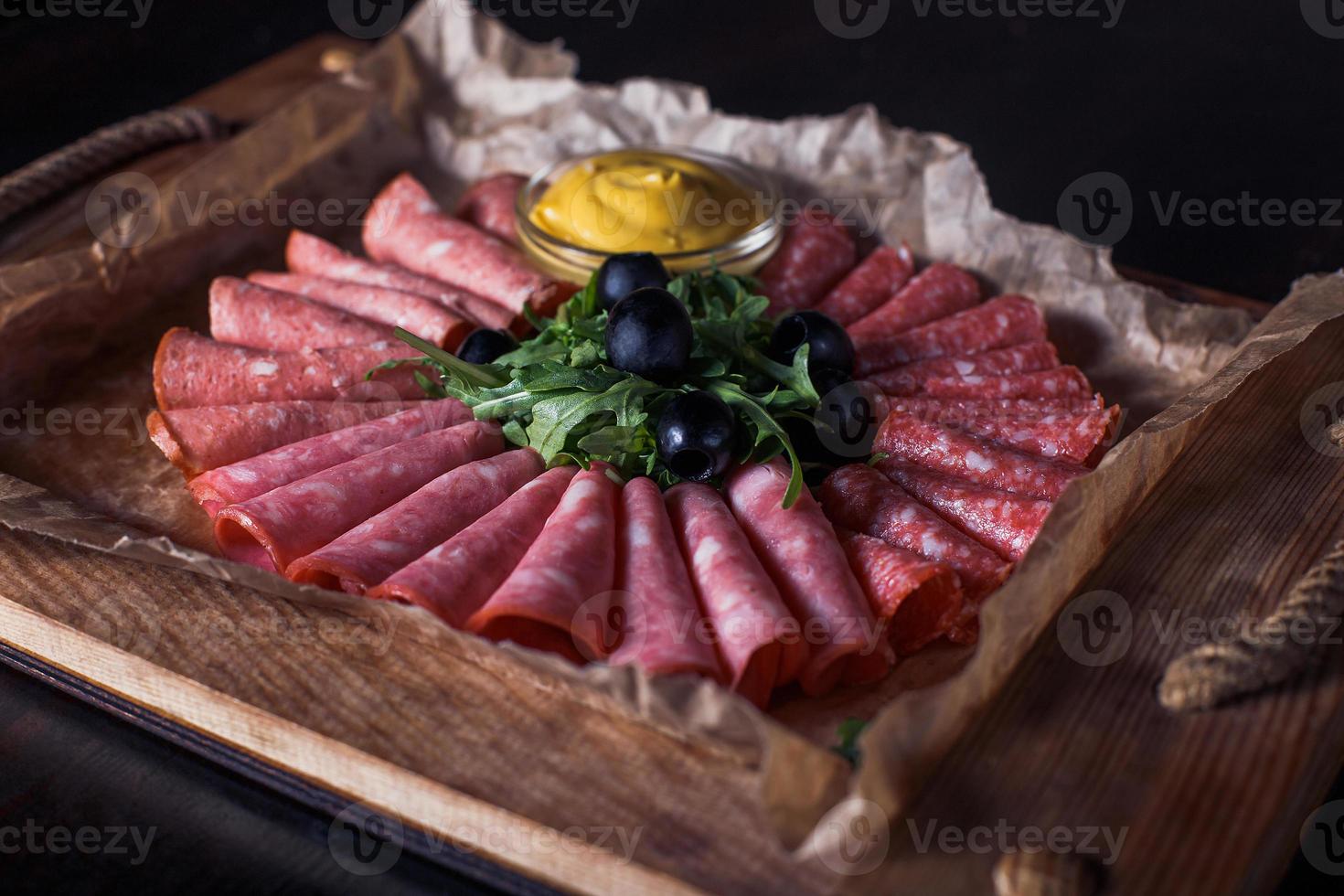 Salchicha cortada con hierbas y salsa en una bandeja de madera, hermosa porción, fondo oscuro foto