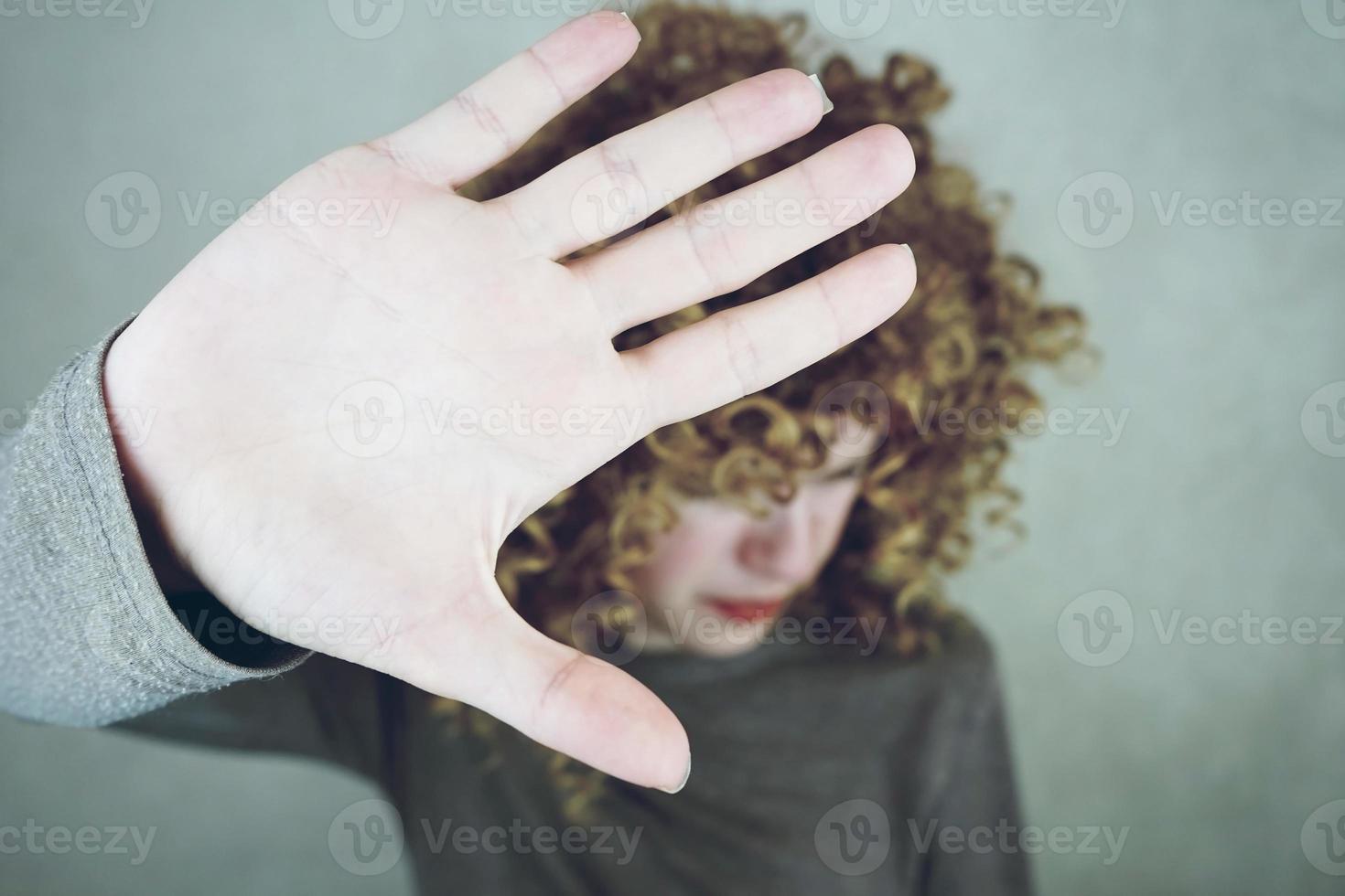 Primer plano de la palma de la mano de una mujer joven y hermosa que cubre su rostro, su cabello es rizado y rubio, se ve enojada o cansada foto