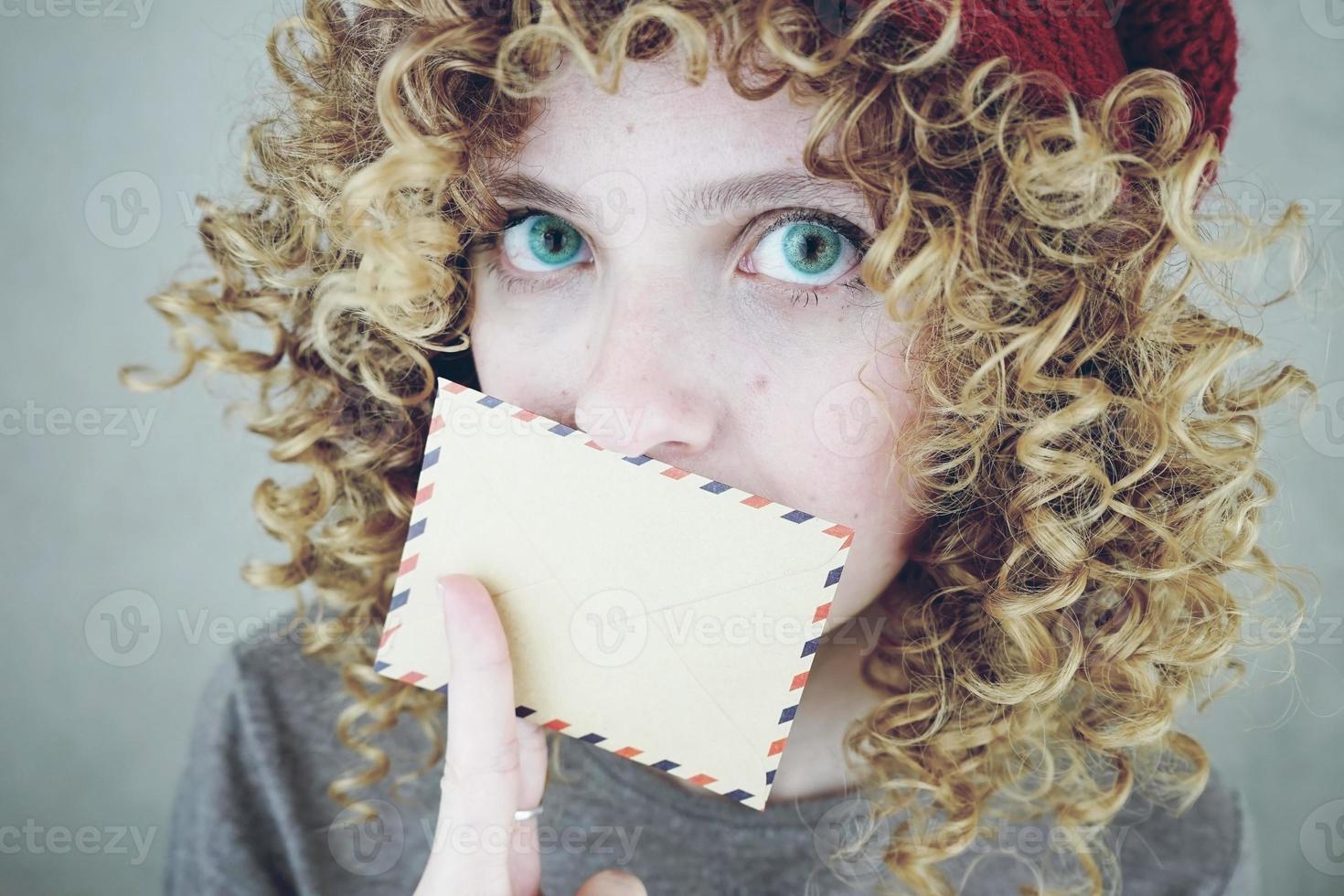 Closeup retrato de una bella y joven mujer divertida con ojos azules y cabello rubio rizado con una carta que sospecha del mensaje foto