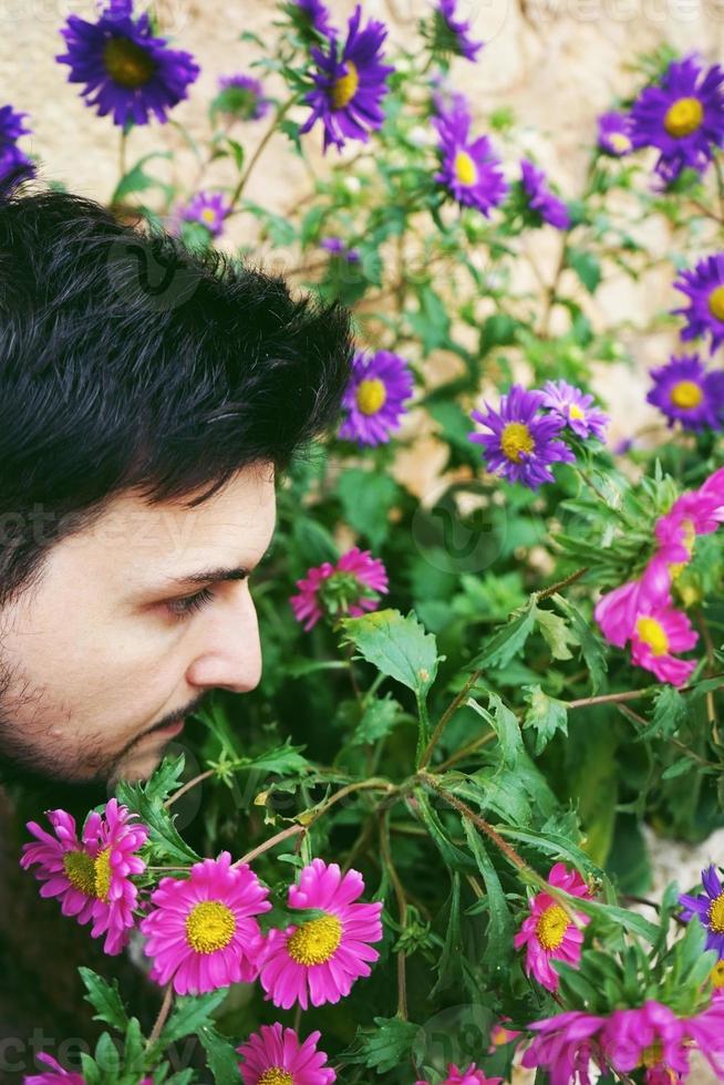 Closeup side view of a young attractive man in calm looking and smelling outdoor flowers photo