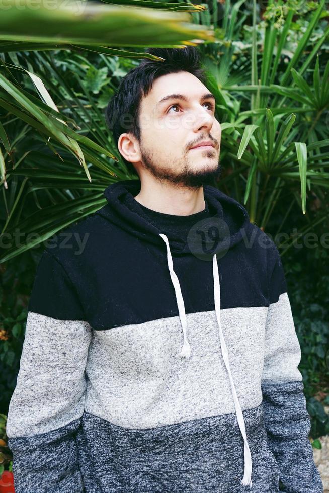 Un joven atractivo en calma de pie y mirando hacia arriba con plantas al aire libre detrás de él foto